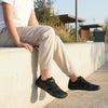 Niña sentada en un muro con zapatillas respetuosas Saguaro Vitality III 2.0 blancas, calzado ligero y transpirable para el tiempo libre.