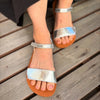 Pies femeninos luciendo las sandalias minimalistas Saguaro Glow I plateadas en exteriores.