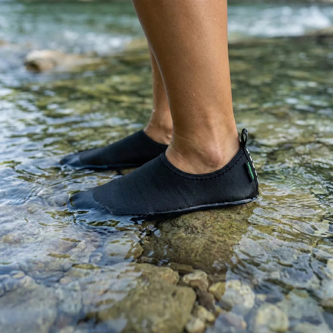 Pies con zapatillas de agua Saguaro negras en agua.